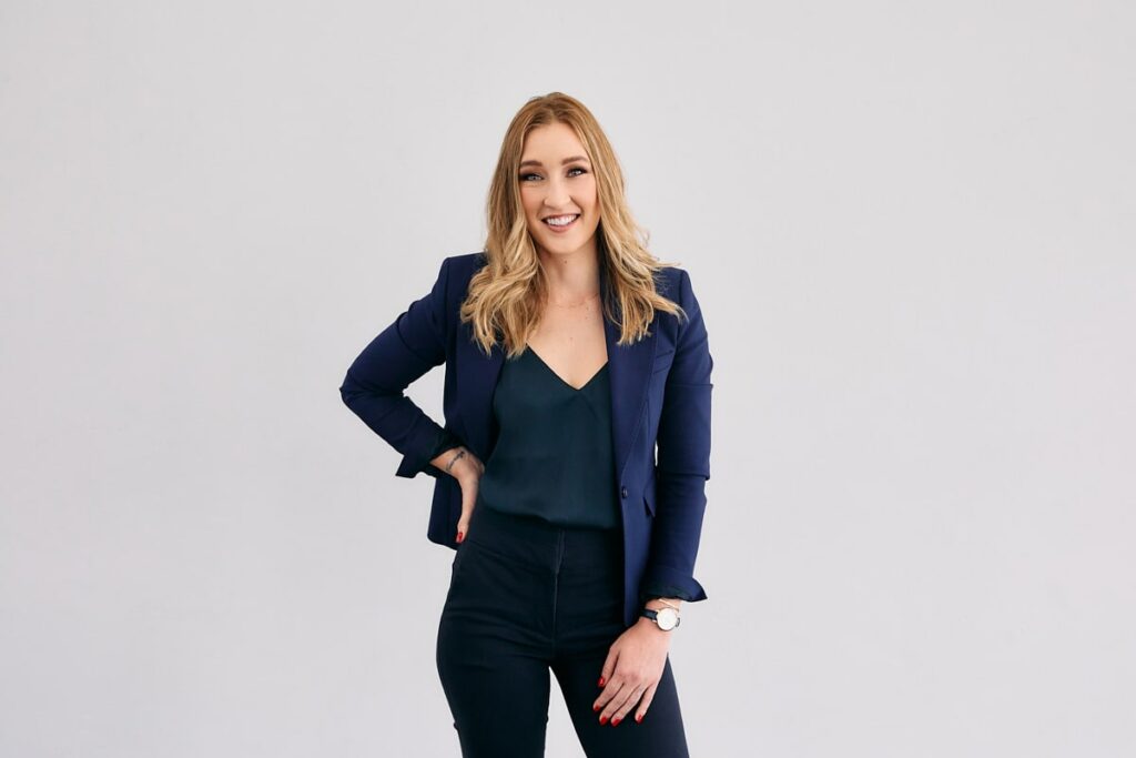 Woman with blonde hair, a black shirt and blue jacket poses for a personal branding portrait